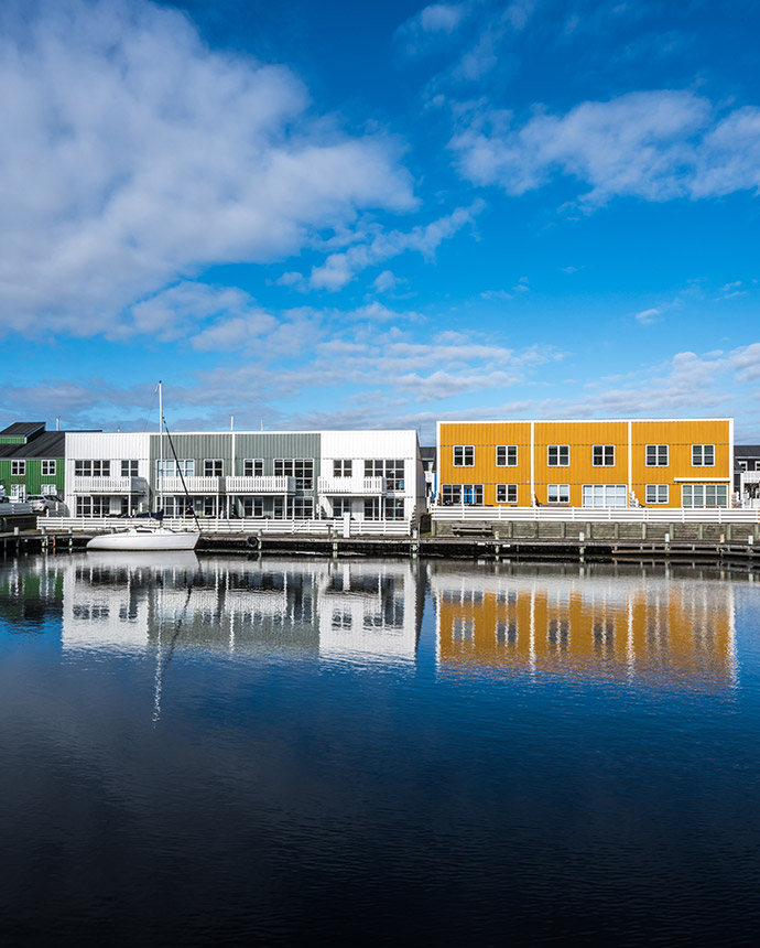 Farbenfrohe Reihenhäuser spiegeln sich in einem ruhigen Hafenbecken. Dieses Bild symbolisiert die Vielfalt an Immobilien, die mit der Wohngebäudeversicherung von Voigt Versicherung geschützt werden können. Prüfen Sie jetzt, wie Sie Ihre Immobilie bestmöglich absichern können.