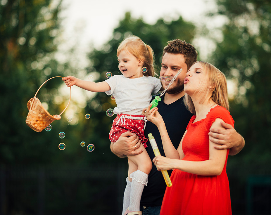 Eine glückliche Familie spielt mit Seifenblasen im Freien. Eltern sichern die Zukunft ihrer Kinder – mit maßgeschneiderten Kinderversicherungen bei Voigt Versicherungen