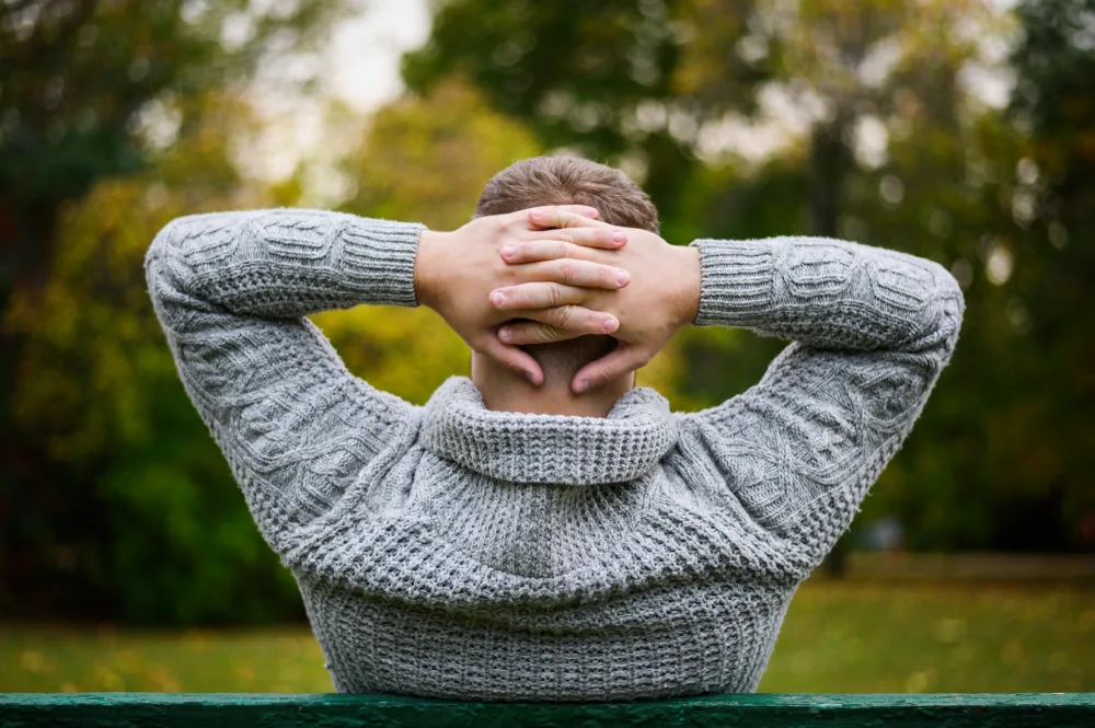 Mann sitzt im Park und verschränkt seine Hände hinter dem Kopf